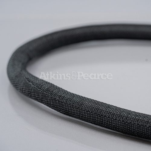A piece of Atkins and Pearce's Standard Enclose® expandable woven sleeving in black, showcased on a gray background, highlighting the sleeving's texture and seamed design. Features the company watermark.