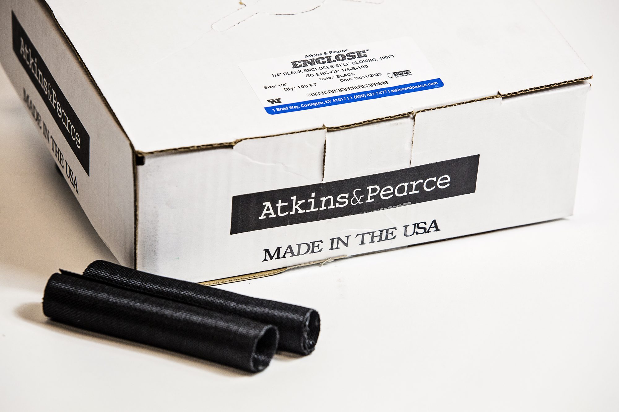 Enclose® woven black sleeving cut pieces sitting next to an e-commerce box packaging option for online purchase.